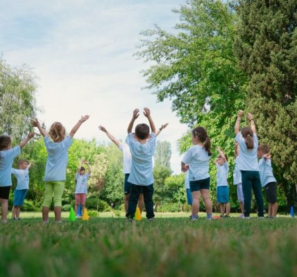 Group of children with instructor doing exercises in a sunny park setting, promoting outdoor activity.