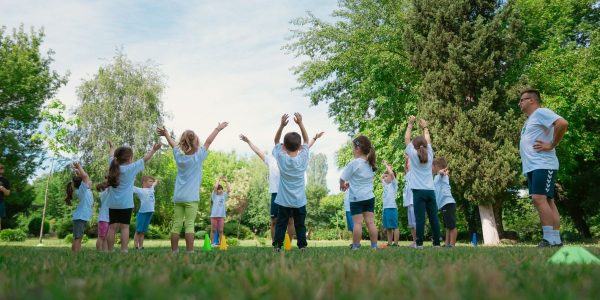 Group of children with instructor doing exercises in a sunny park setting, promoting outdoor activity.
